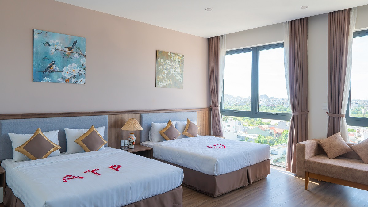 Một góc phòng ngủ khách sạn với giường lớn, chăn ga cao cấp và cửa sổ nhìn ra thành phố